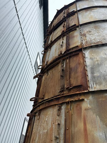 Close-up of a rusted metal silo beside a corrugated metal building.