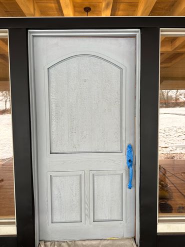 A white front door with a blue plastic-covered handle under a wooden porch roof.