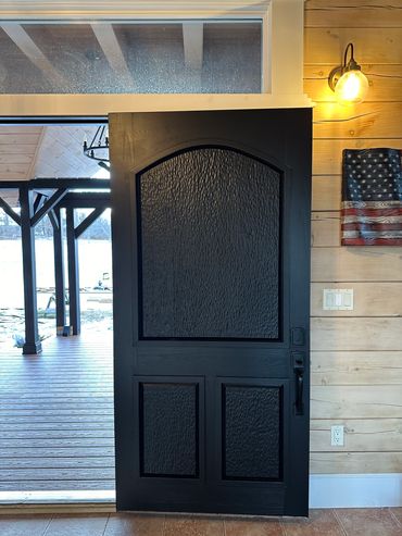 Black textured front door partially open with wooden porch and rustic interior.