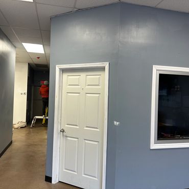 Office hallway with white doors and a person on a ladder in the background.