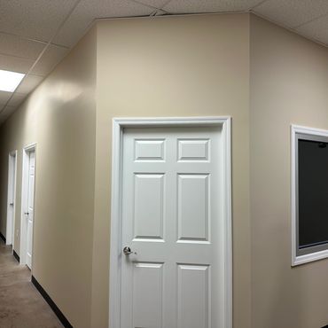 Interior hallway with white doors and beige walls under fluorescent lighting.