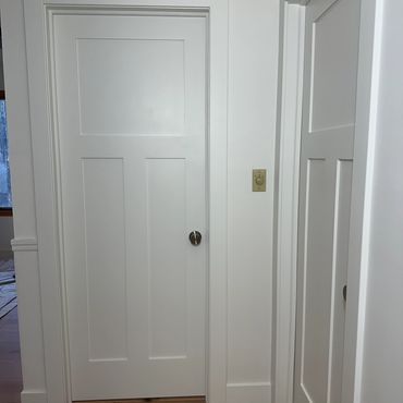Two white paneled doors in a hallway with wooden flooring.