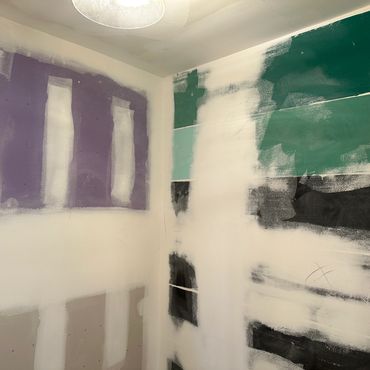 Partially painted walls with patches of purple, green, and black in a room under renovation.