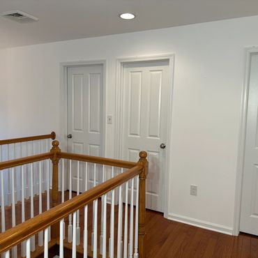 A hallway with three white doors and wooden railing overlooking stairs.