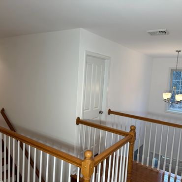 Interior hallway with wooden railing, white walls, and a hanging light fixture near a window.