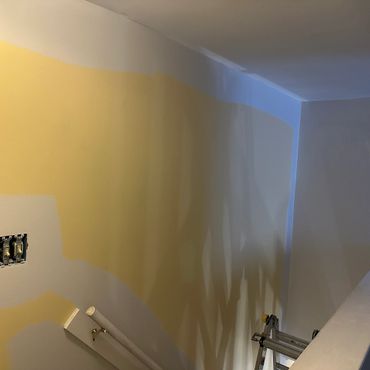 Wall partially painted from yellow to white with ladder nearby.