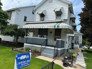 White house with green-striped awnings and painting equipment on the lawn.