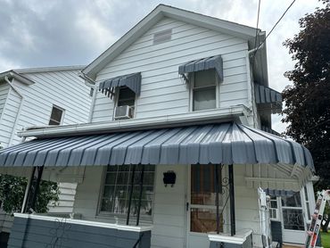 White house with blue metal awnings over windows and porch.