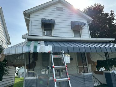 House awning being painted in multiple colors with a ladder and paint bucket.