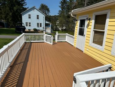 Spacious wooden deck with white railings attached to a yellow house.