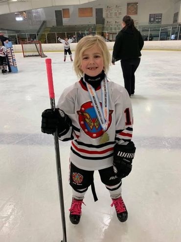 A young girl holding a hockey stick and medal.