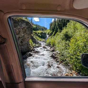 View of a flowing river and greenery through a car window.