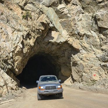A car parked in front of a rocky tunnel entrance.