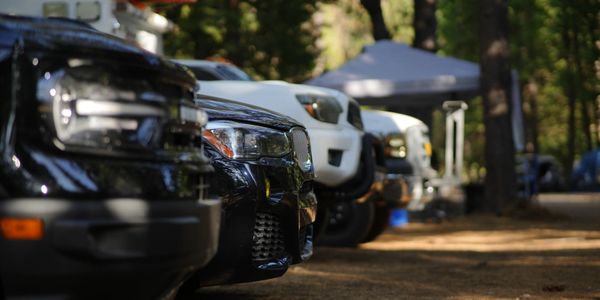 Close-up view of several parked trucks in a forested campsite.