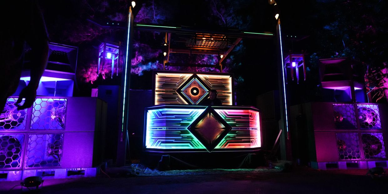 Colorful illuminated DJ booth with vibrant lights in a dark outdoor setting.