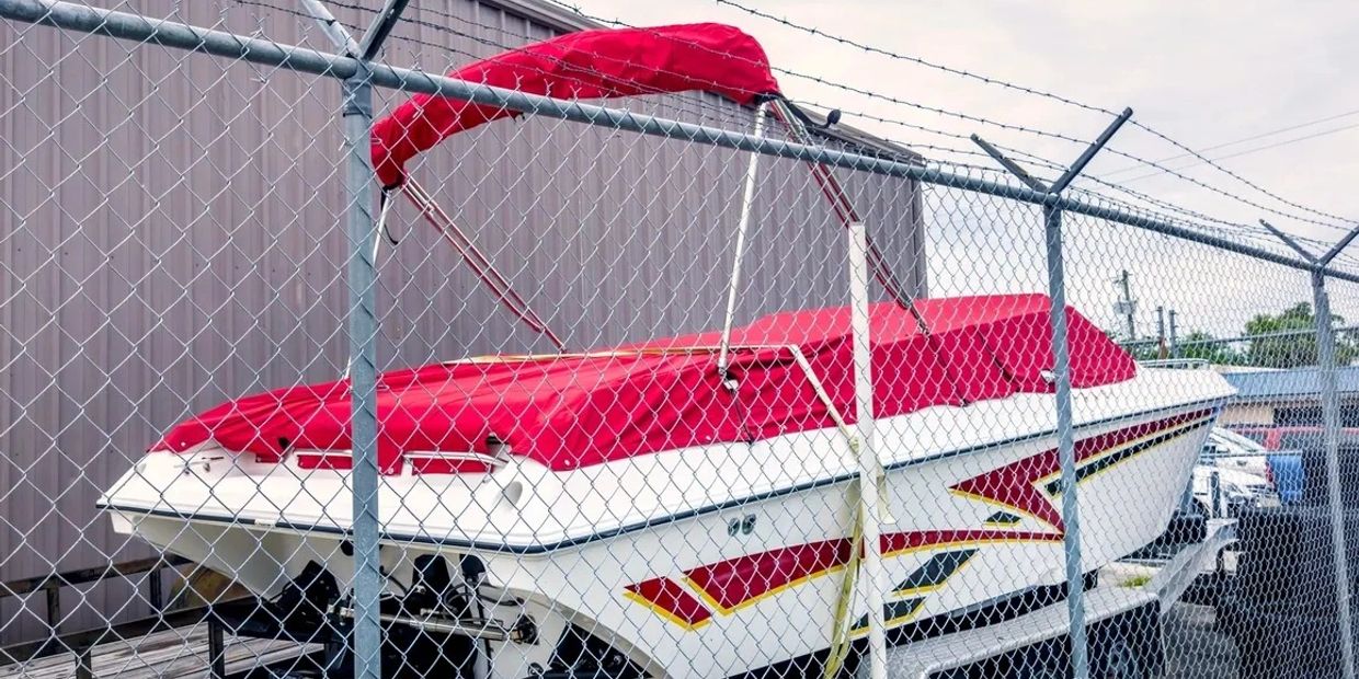 White and red boat behind a chain-link fence.