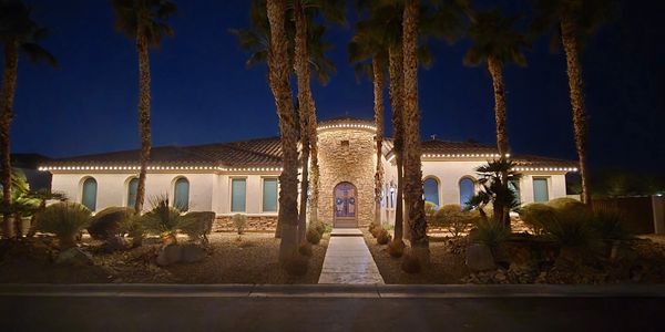 A beautifully lit house at night with palm trees lining the walkway.