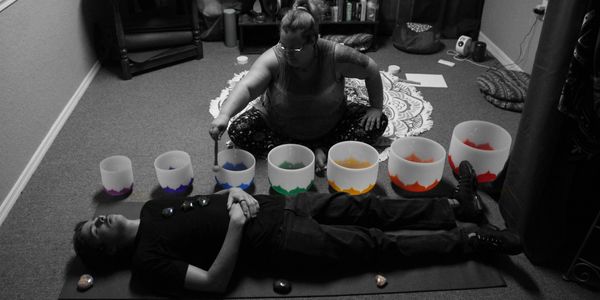 A person conducts a sound healing session with crystal bowls and a lying participant.