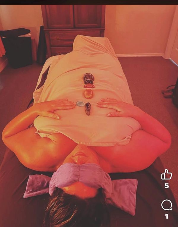 Person lying down with healing stones on their body and a lavender eye pillow.
