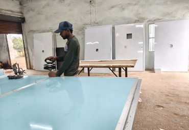A man working on a large glass panel in a workshop with doors in the background.