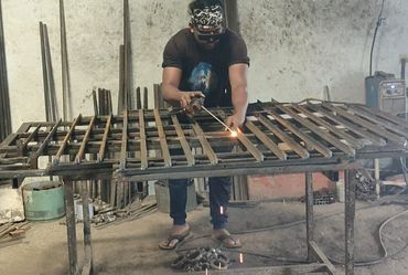Man welding metal bars on a large table in a workshop.