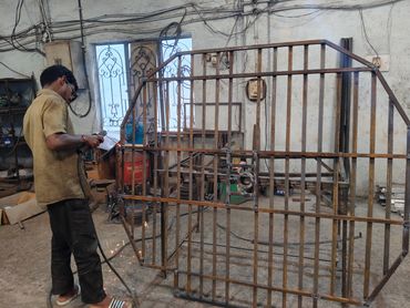 A man welding a metal gate frame in a workshop.