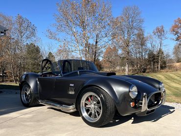 Sleek black classic sports car parked on a driveway under clear blue skies.