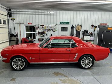 A shiny red classic Ford Mustang parked inside a clean garage.
