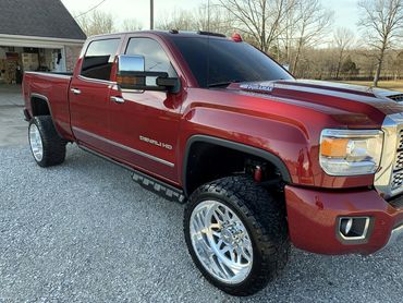 Shiny red Denali HD truck with large chrome wheels and tinted windows.