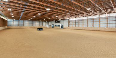 Spacious indoor arena with sandy floor and wooden ceiling beams.