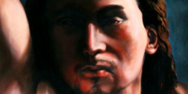 A close-up portrait of a man with long hair in dramatic lighting.