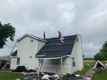 Two workers on a roof installing new shingles on a cloudy day.