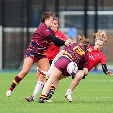 Women playing rugby, one tackling with intensity.