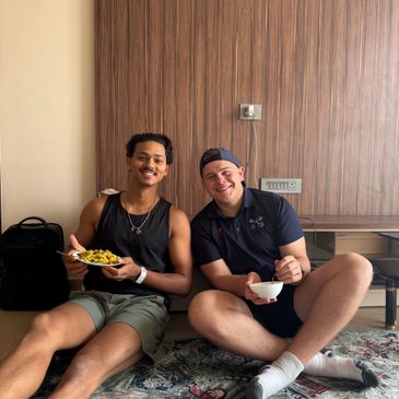 Two friends sitting on the floor enjoying food together.