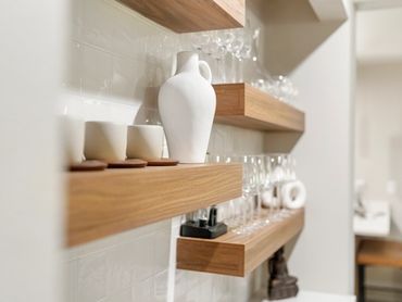 Minimalist wooden shelves with white pottery and glassware in a modern kitchen.