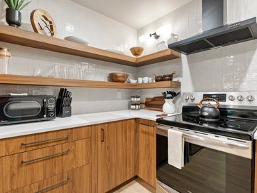 Modern kitchen with wooden cabinets, open shelves, and stainless steel stove.