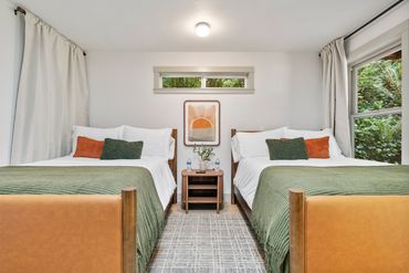 Symmetrical bedroom with two beds, green and orange pillows, and a central nightstand.