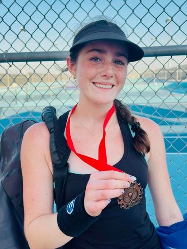 SCHP Tennis player smiling with a bronze tournament medal courtside