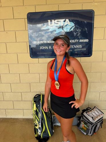SCHP Tennis player with tournament medal beside USTA Outstanding Facility Award sign