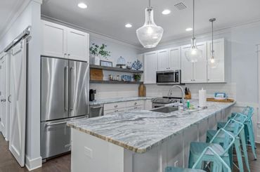Modern kitchen with marble countertops, white cabinets, and teal bar stools.