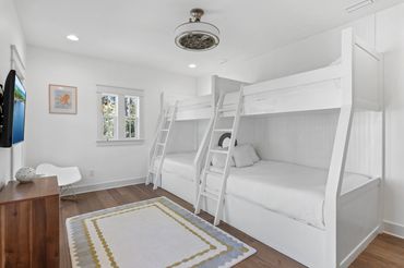 Bright bedroom with white bunk beds and wooden flooring.
