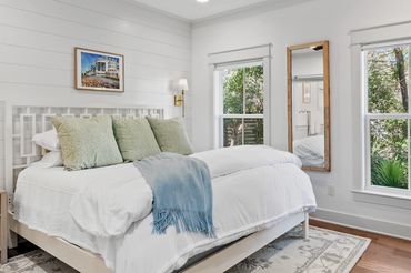 Bright bedroom with white walls, large windows, and a cozy bed.