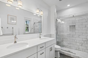 Bright modern bathroom with double sinks and marble shower.