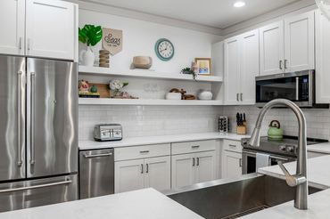 Modern white kitchen with stainless steel appliances and open shelves.