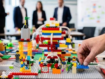 Manos construyendo con bloques de LEGO en un entorno de oficina.