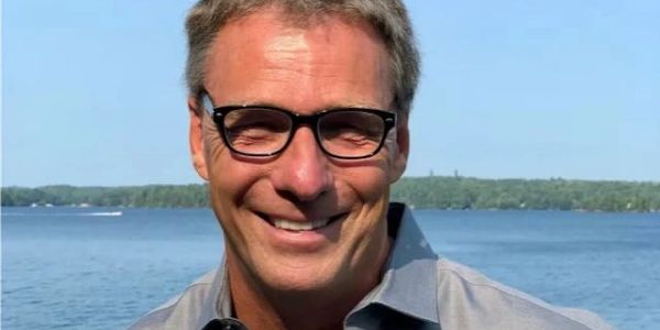 Smiling man with glasses by a lake.