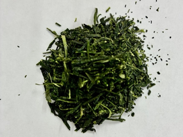 Pile of dried green tea leaves on a white surface.