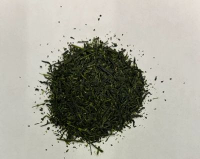 Pile of dried green tea leaves on white surface.