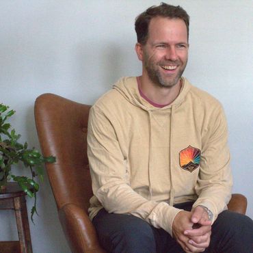 Smiling man in beige hoodie sitting in a brown leather chair.