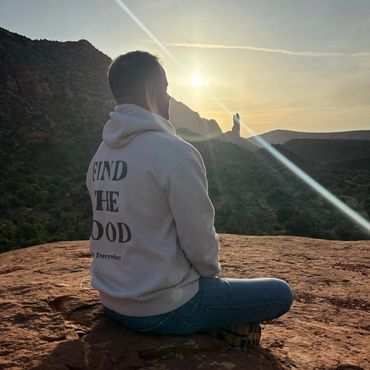 Person sitting on a rock at sunset, holding the sun in their hand.